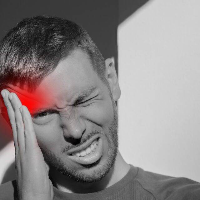 Young man touching his temple and having strong tension headache. Cluster headache. Man suffering from migraine, stress, hangover with red alert accent. Hands on head. High quality photo
